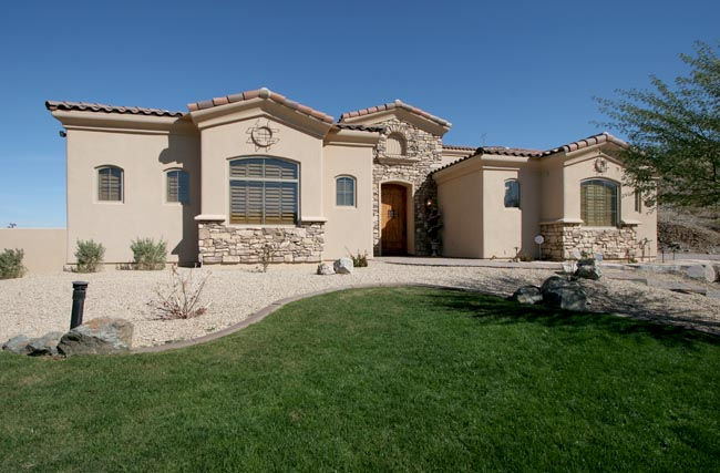 Front of classic stucco home with stone features and grass lawn