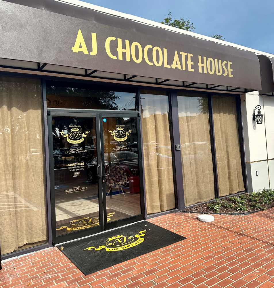 brown awning with gold letters that says aj chocolate house and glass entrance doors with brick walkway
