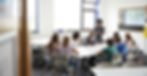 Students and teacher engaged in an interactive classroom discussion with natural light streaming in