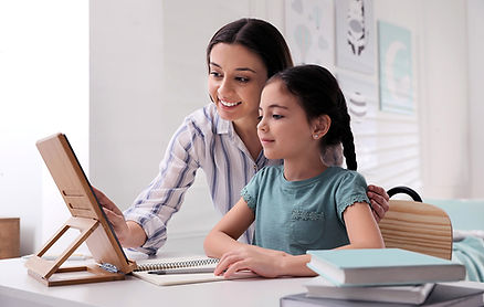 mother helping her daughter doing homework on laptop tablet