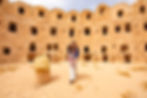The author walking toward the camera from the small windows in a mud interior with a bumpy top that looks like lace in Qasr Al-Haj, Libya.