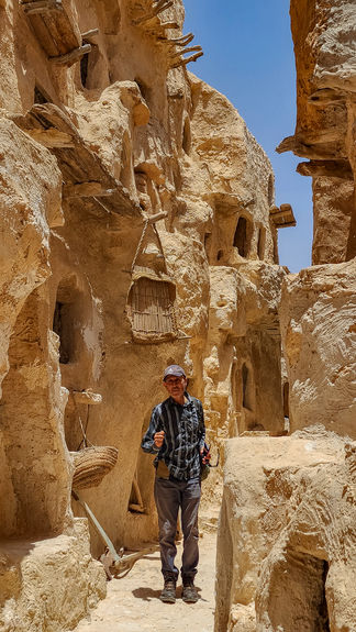 Tour guide, Abdul Rahman walking through two mud and stone walls with windows cut into them where food commodities were stored in Qasr Al-Nalut in Libya.