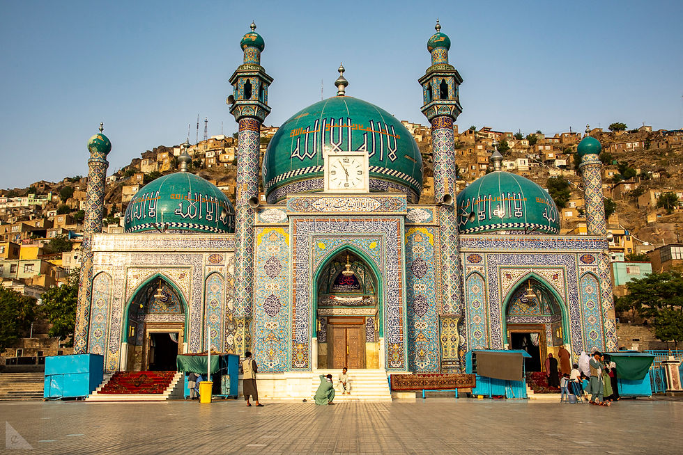 The mosque Rawza Sakhi Shah-e-Mardan with turquoise domes, elaborate tiles has four visible minarets and three large domes from this symmetrical front view. On the steps of the mosque are two men taking photos. To the right is the women's prayer hall entrance, and the mens' is to the left.