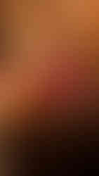 A colorfully clothed man making almond tea in Ghadamès, Libya by pouring the tea from one pot to another in order to aerate it and mix in sugar. His tea shop is colorful with pots and woven carpets and wall coverings behind him.