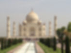 Taj Mahal with its white marble domes and four minarets, surrounded by gardens and a reflecting pool. Visitors are gathered near the entrance.