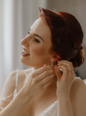 Hochgesteckte Brautfrisur während die Braut ihre Ohrringe anlegt, elegantes Braut Make-up