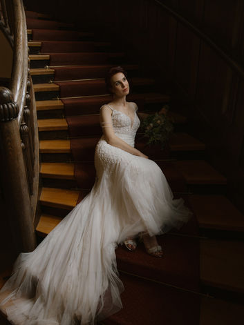Braut mit eleganter Hochsteckfrisur und fließendem Brautkleid sitzend auf einer Treppe