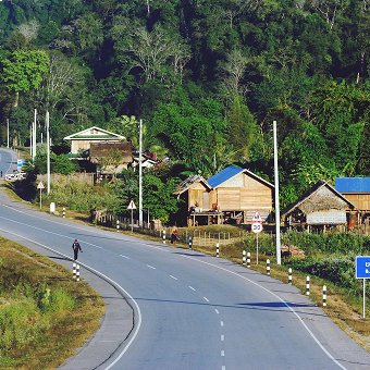 Winding road in a rural landscape with houses and a walking person