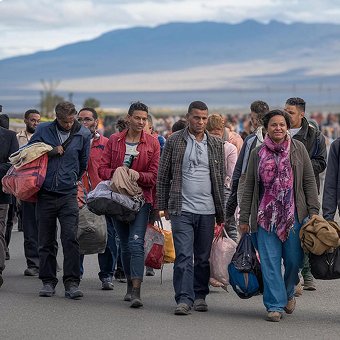 People carrying bags walk on a road with mountains