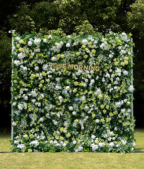 Elegant white rose flower wall with light greenery, standing on grass with a forest background, perfect for weddings and formal events.