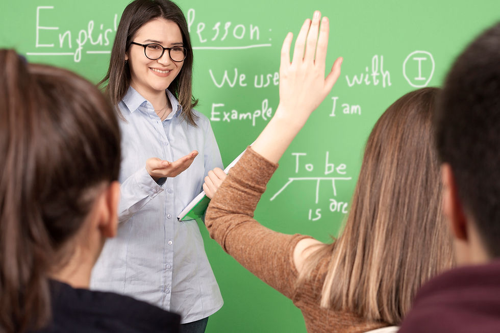 Teacher in front of chalk board. Student raising hand.