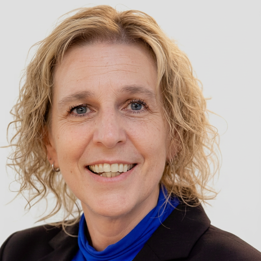 Studio photography of a smiling woman with blonde curly hair. She wears a dark blazer and a blue top, looking directly at the camera.