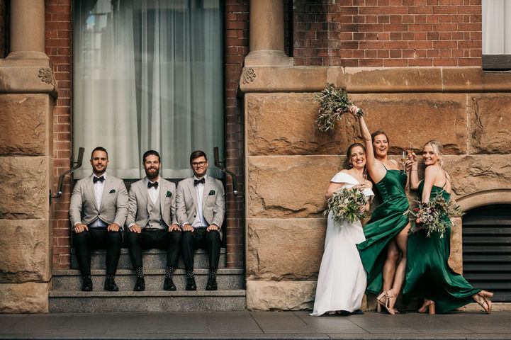 Bridal party in green dresses seated on stone steps at a Sydney heritage venue.
