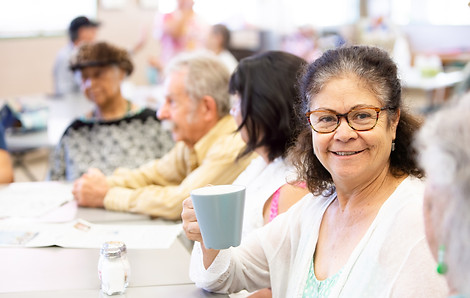 Older adults sharing coffee and conversation at a community table.