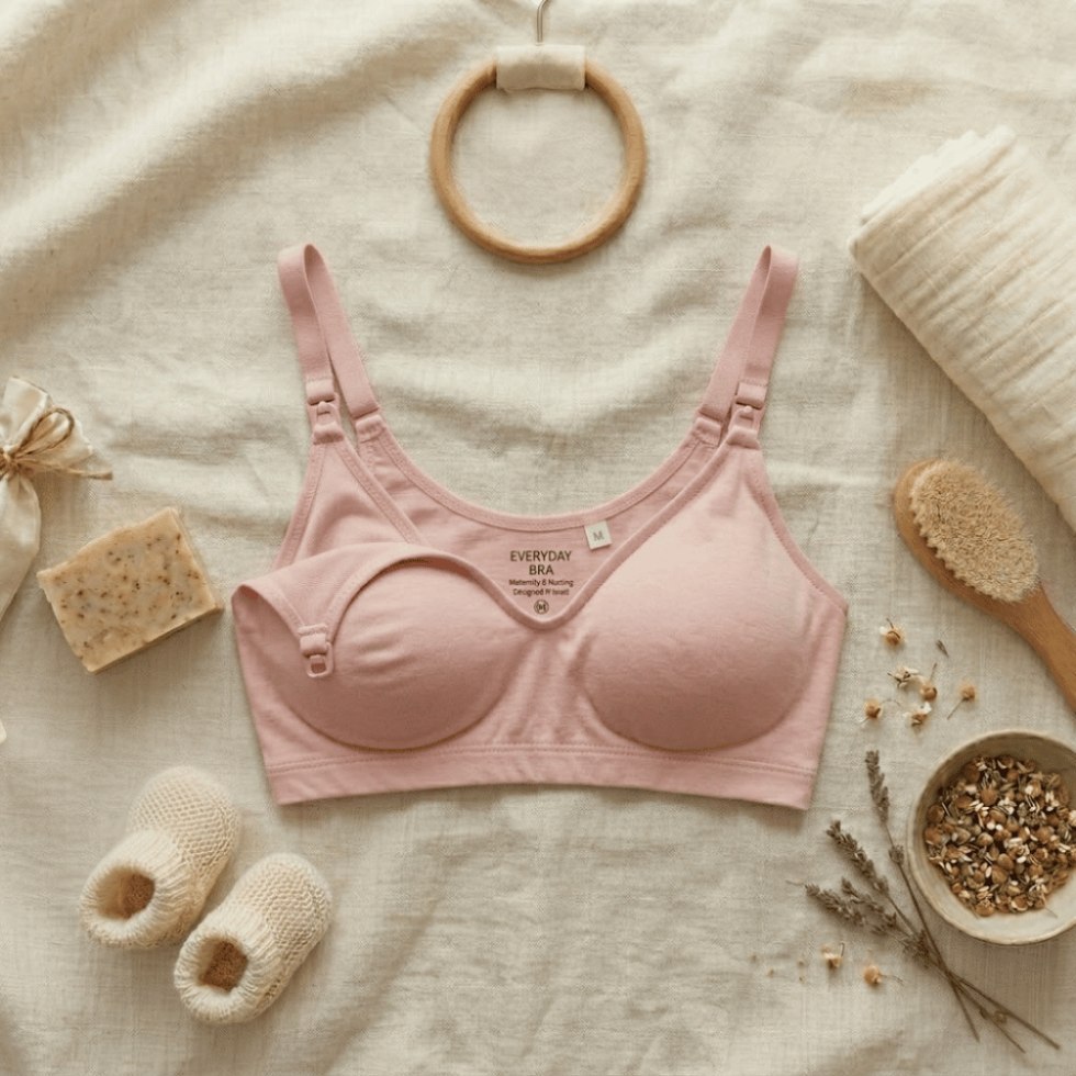 The Yael seamless nursing bra in chalk pink by Yael and Michal, flat lay on cream linen with baby booties and dried flowers
