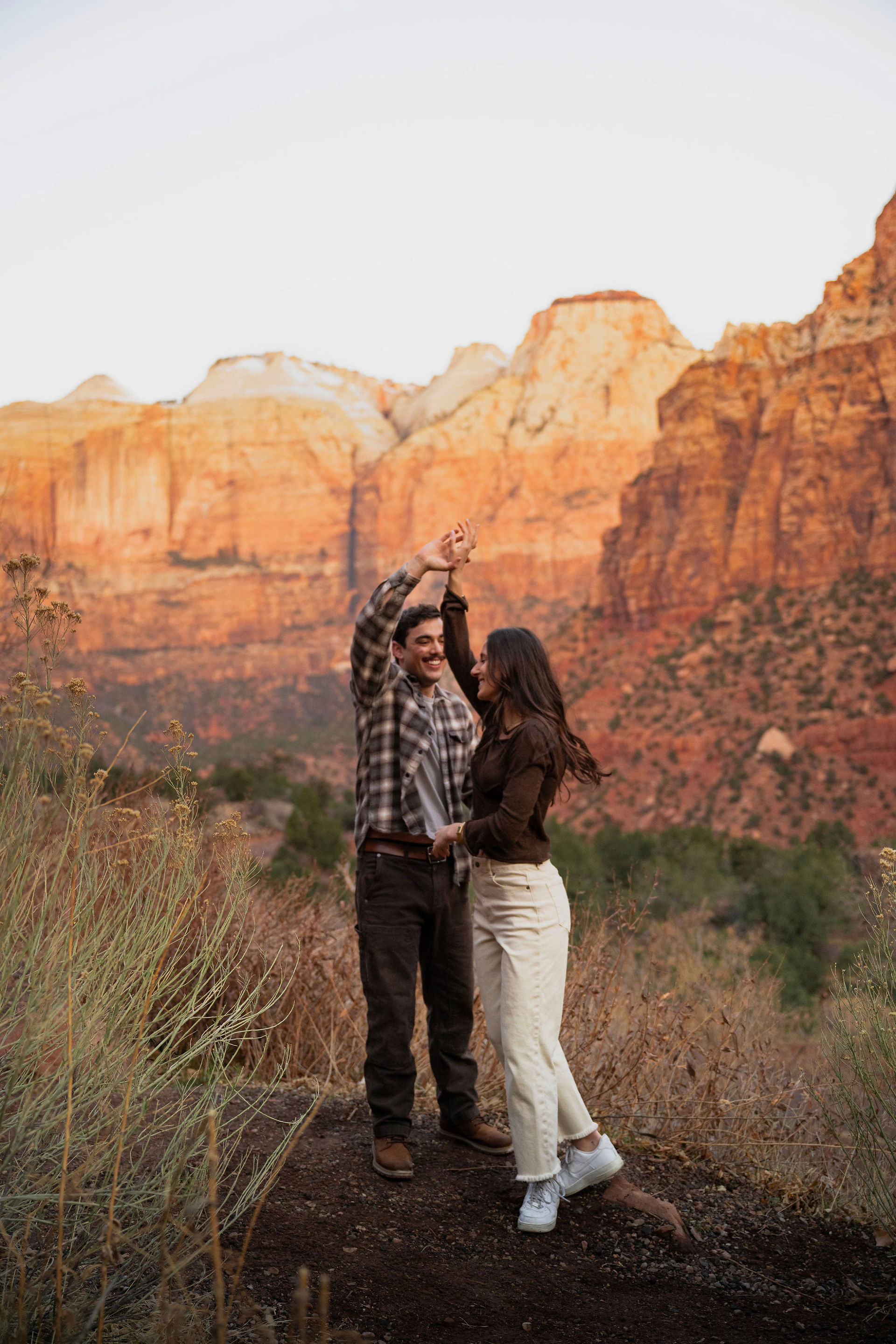 couple dancing and twirling in the desert with tall rocky cliffs in the background at sunrise in zion national park 