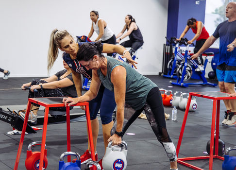 Fitness instructor assists client with kettlebell exercise, action photography