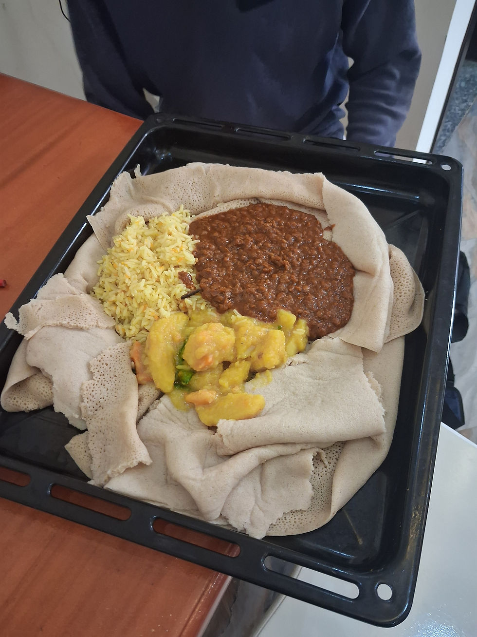 This is a typical meal for us. Injera is the spongy base layer. Everything in Ethiopia is eaten on Injera. They do not have utensils, but rather pull this off and use it to scoop the other items that are lying on it, and then we eat it. This plate has potatoes and then lentils, which are also very common and eaten at almost every meal.