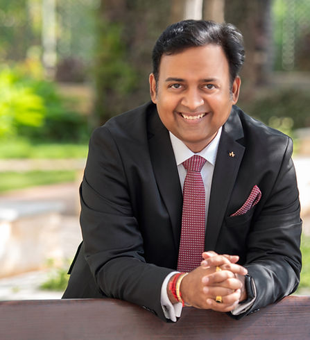 Man in a black blazer and red tie smiling in a lush outdoor setting