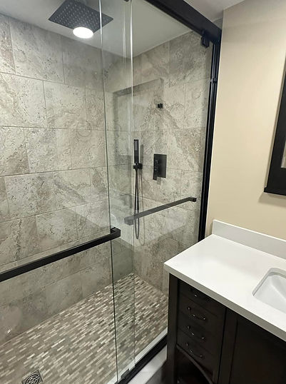 A modern walk-in shower with black hardware and beige stone-look tiles in a Pottstown bathroom.