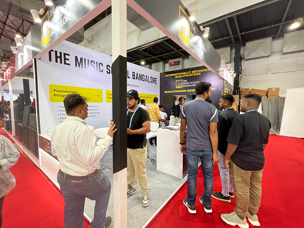 People gather at The Music School Bangalore booth at a trade show, with bold signage and red carpeted aisles.