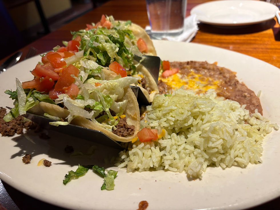 Plate of tacos with lettuce and tomatoes, rice, and refried beans on a restaurant table, warmly lit and appetizing.