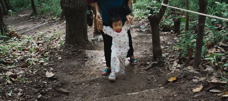 Woman helping a toddler walk up dirt stairs in a forest