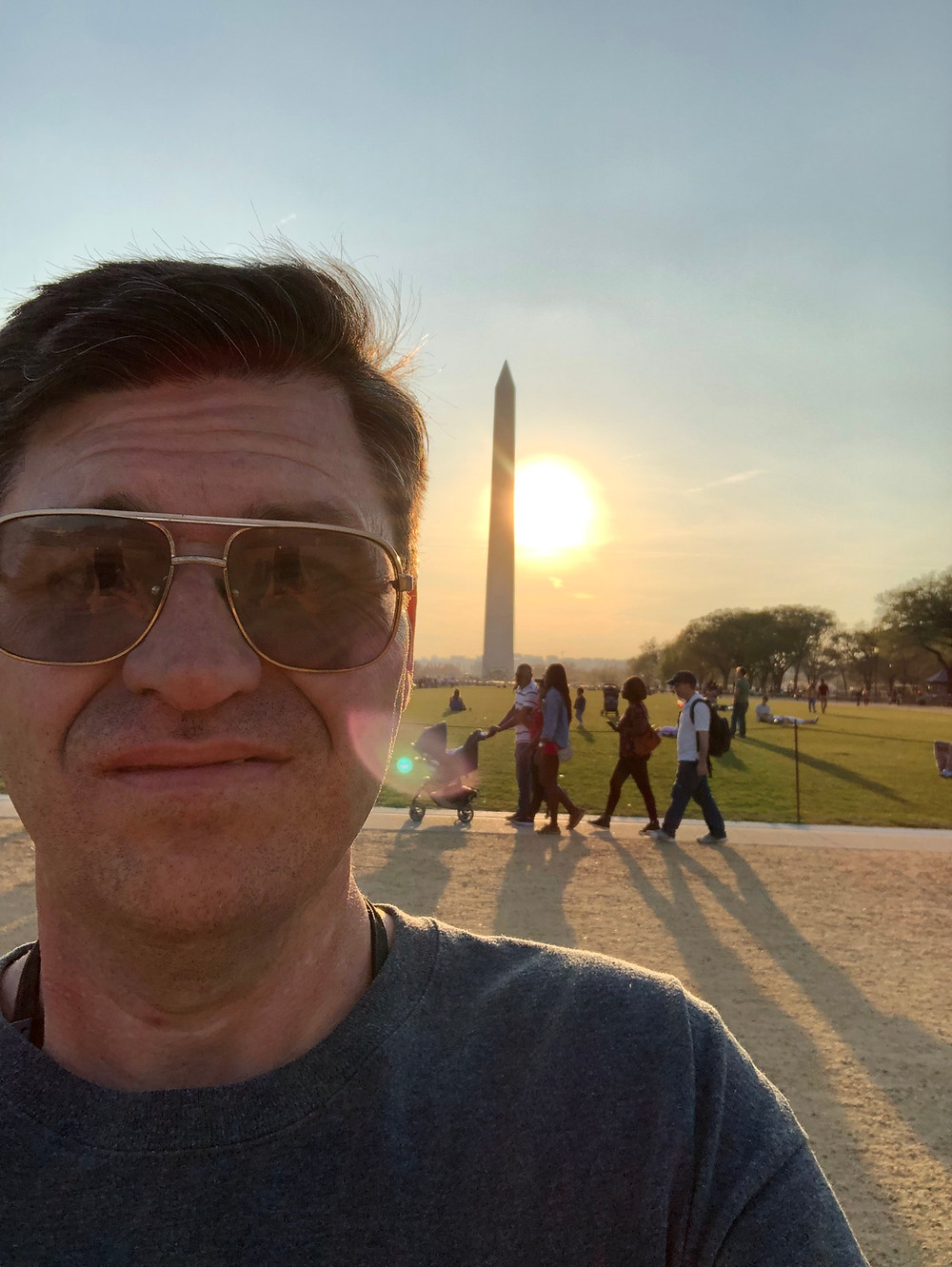 Selfie of Mike, wearing aviators with the Washington Monument and the sun setting behind him