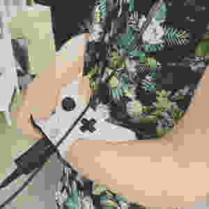 Brian Marquez is playing a video game with both his hand and his arm on the remote control. Brian is wearing a fantastic Yoshi Hawaiian style button-down shirt.
