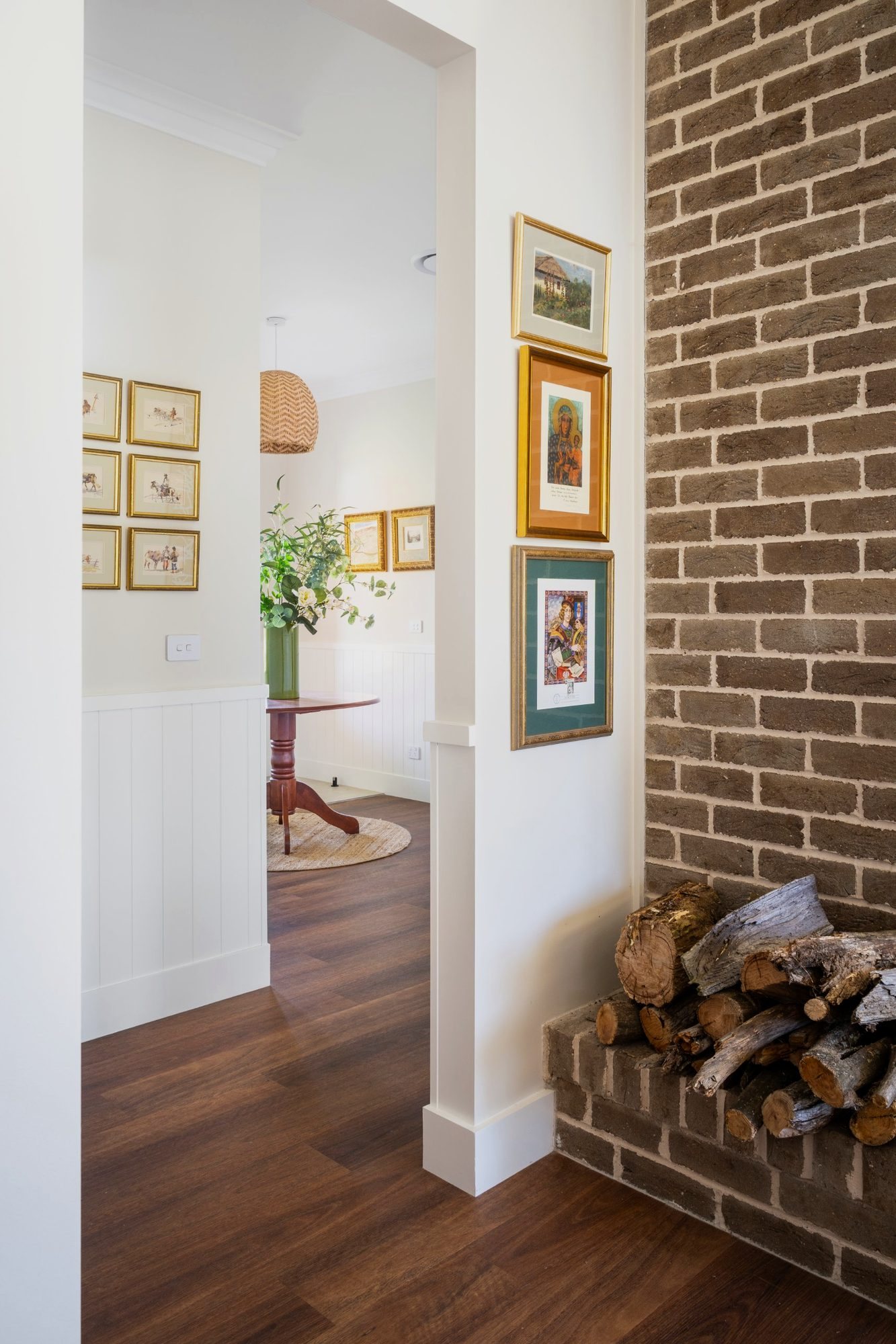 Hallway with exposed brick wall, firewood nook and framed artworks opening to a dining room