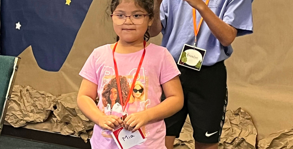 A young girl is standing in front a teen boy, who is holding a piece of paper that says "Monkey."