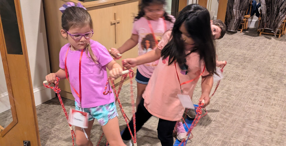 Four children are participating in the "Plank Walk" activity, where there are two wooden boards under their feet. As you walk, you have to pull the board under the correct foot up with a rope that is attached. These children are alternating which foot they try to lift.
