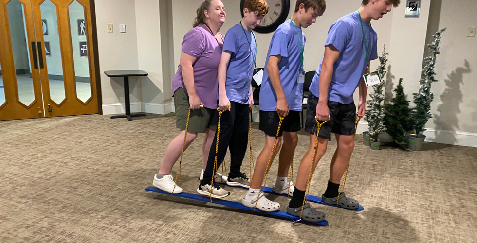 From left to right, an adult woman and three teen boys do the Plank Walk activity. The boy farthest to the right has his mouth open in excitement.