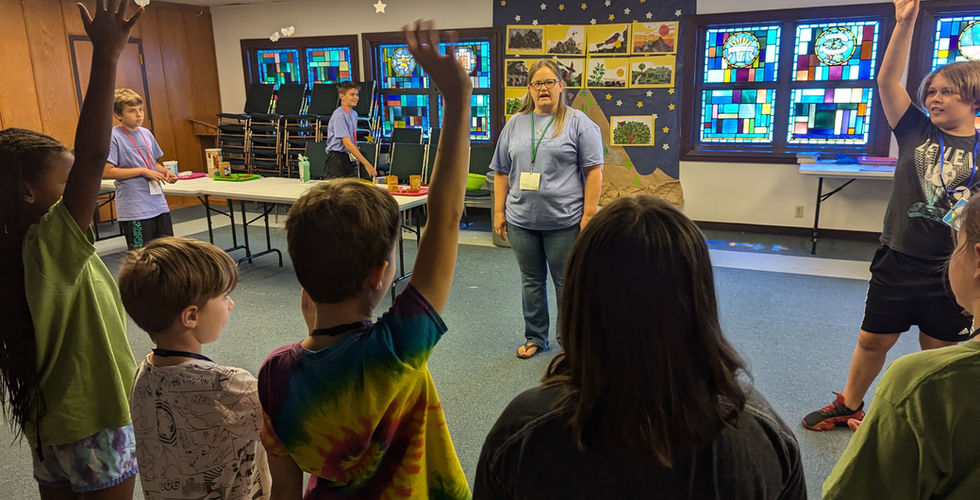 There is a line of five children in mostly shadows looking at adults and teenagers in front of them. A few of them have hands raised.