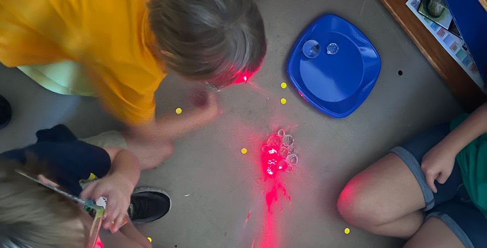 A group of children look on as one youth shines a red laser into a pile of crystals, while the light goes everywhere.