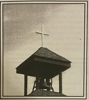 A grainy photo of a bell tower with a cross on top