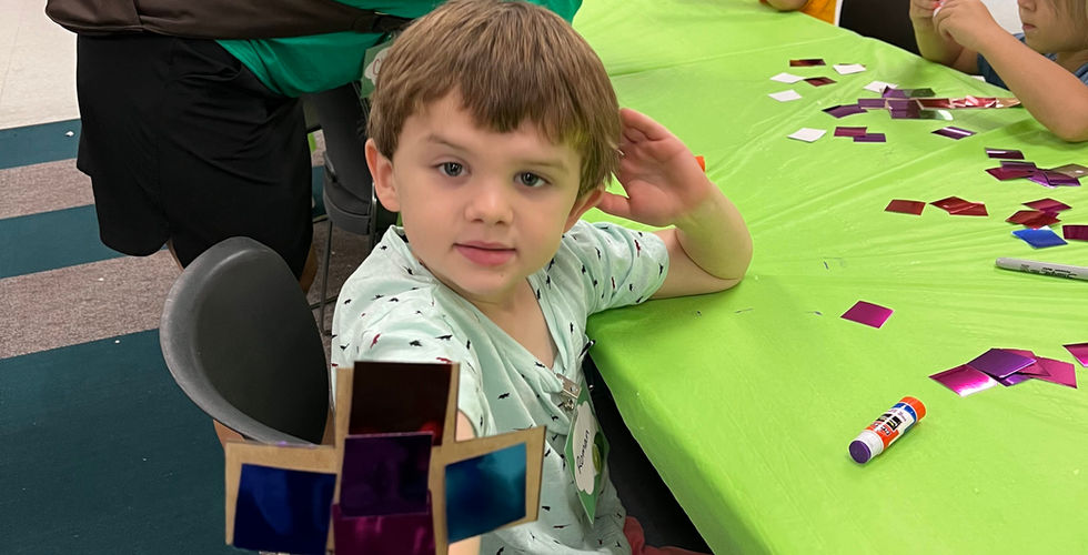 A young boy holds out a cross covered in shiny foil squares