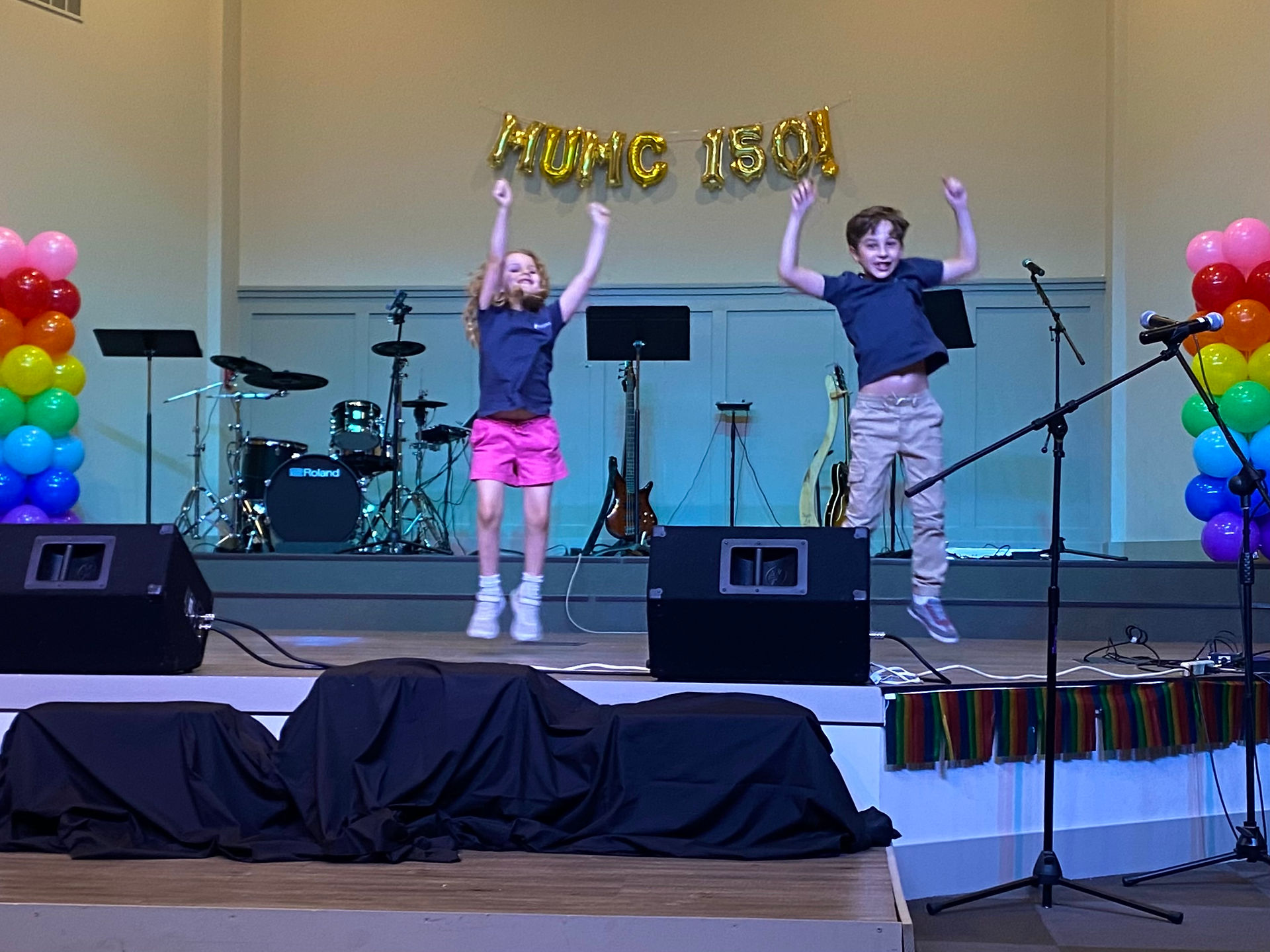 Two kids in matching blue shirts have their hands up, mid jump.