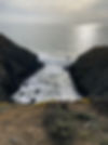 Pacific Ocean with two rocky cliffs on either side of an inlet, sun on the water