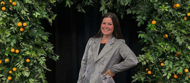 Breanna Mueller Silver Executive VP at Bravenly Global conference event standing under floral arch