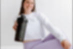 Smiling woman in white top and lilac leggings holds black shaker bottle reading PURPOSE over PERFECT in a bright room
