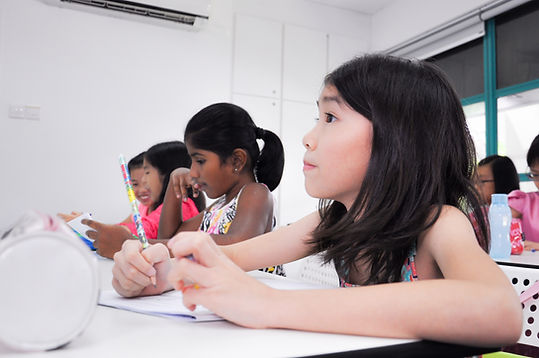 Girl listening attentively to her teacher during his Primary School Writing Enrichment Class for techniques to write a good composition.