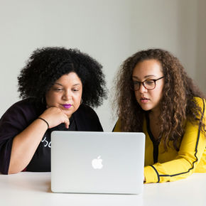 Two Black women work together on a laptop
