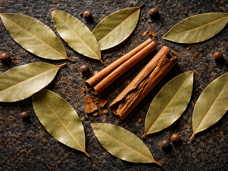 Nahaufnahme von getrockneten Lorbeerblättern und Zimt auf dunklem, strukturiertem Hintergrund mit warmem Licht