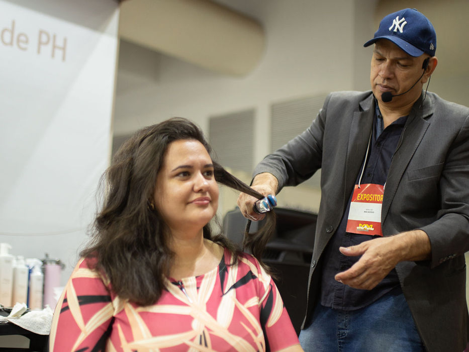 Cabeleireiro alisa cabelo de mulher durante evento feira de beleza com Solliê Professional.