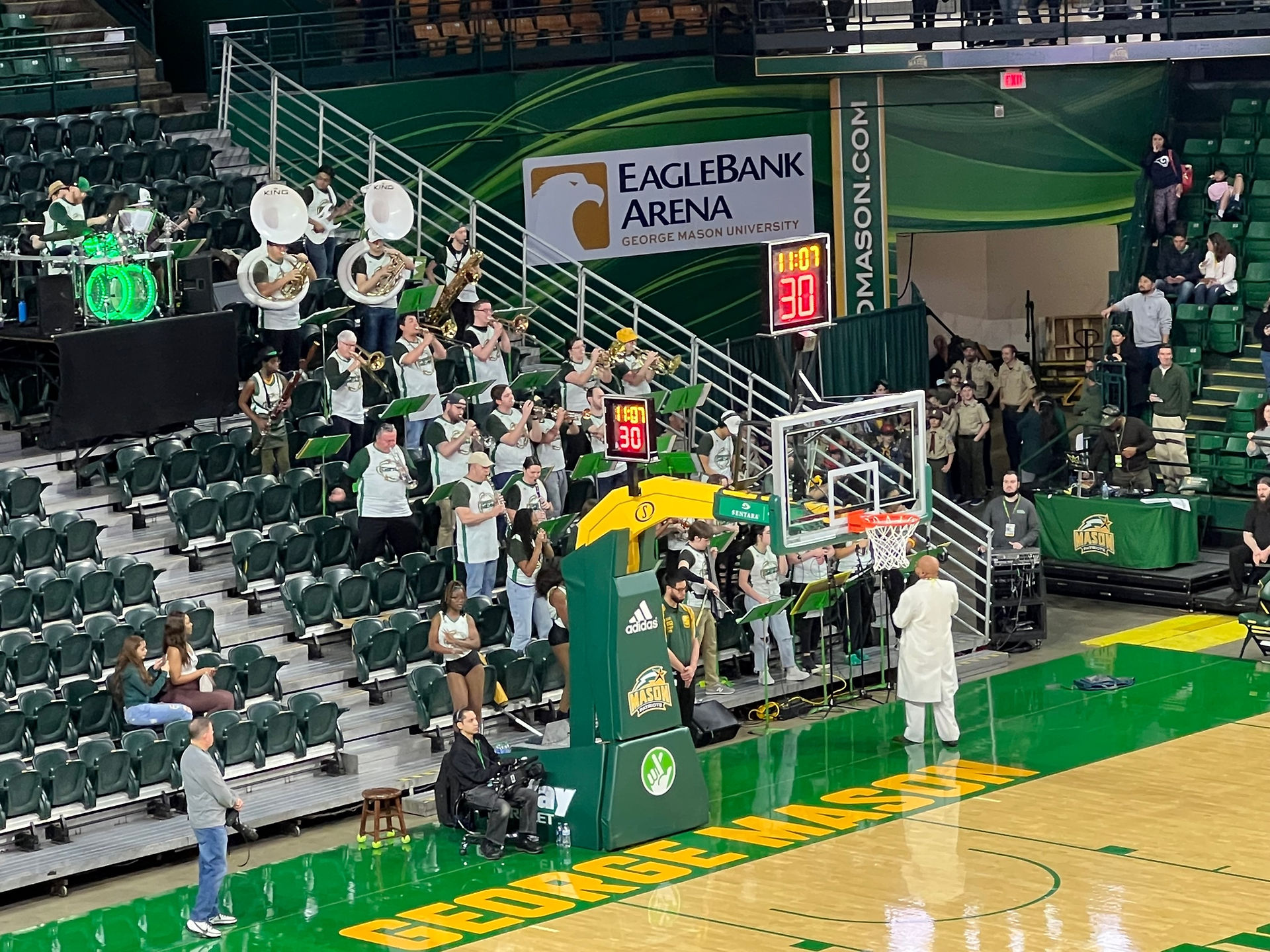 Doc Nix conducting the Green Machine, the George Mason band. Doc Nix is wearing a white suit and holding a scepter and the band is wearing basketball jerseys. 