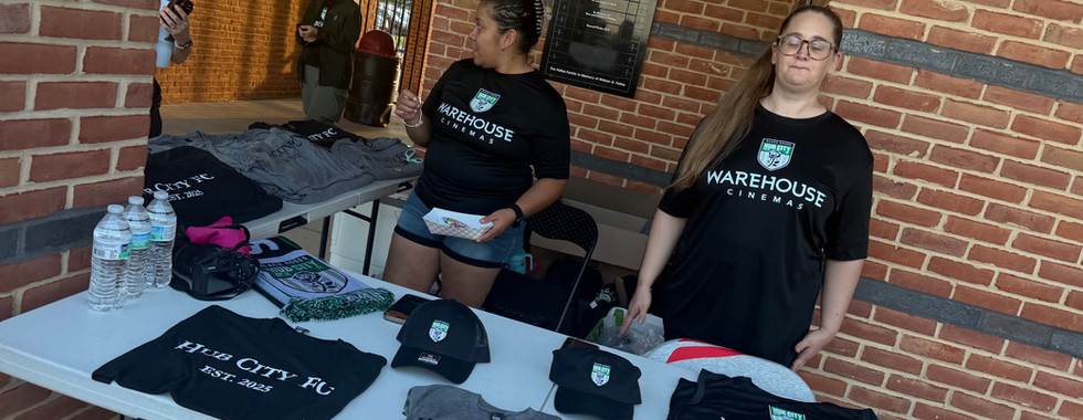 Two women work a merchandise table selling Hub City FC merchandise.