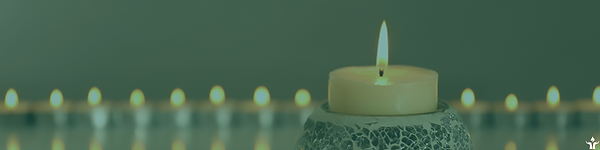 A lit beeswax pillar candle appears in the foreground. A row of lit beeswax tealights appear, very blurrily, in the background.