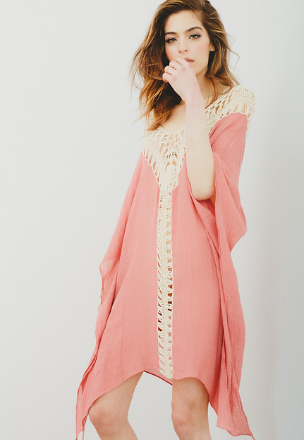 A model poses in a pink cotton gauze dress with her hand touching her lip