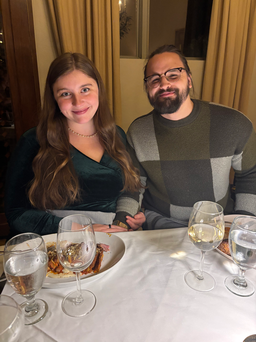 Couple smiling at dinner with wine glasses and plates on the table.